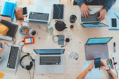 People sitting down near table with assorted laptop computers.