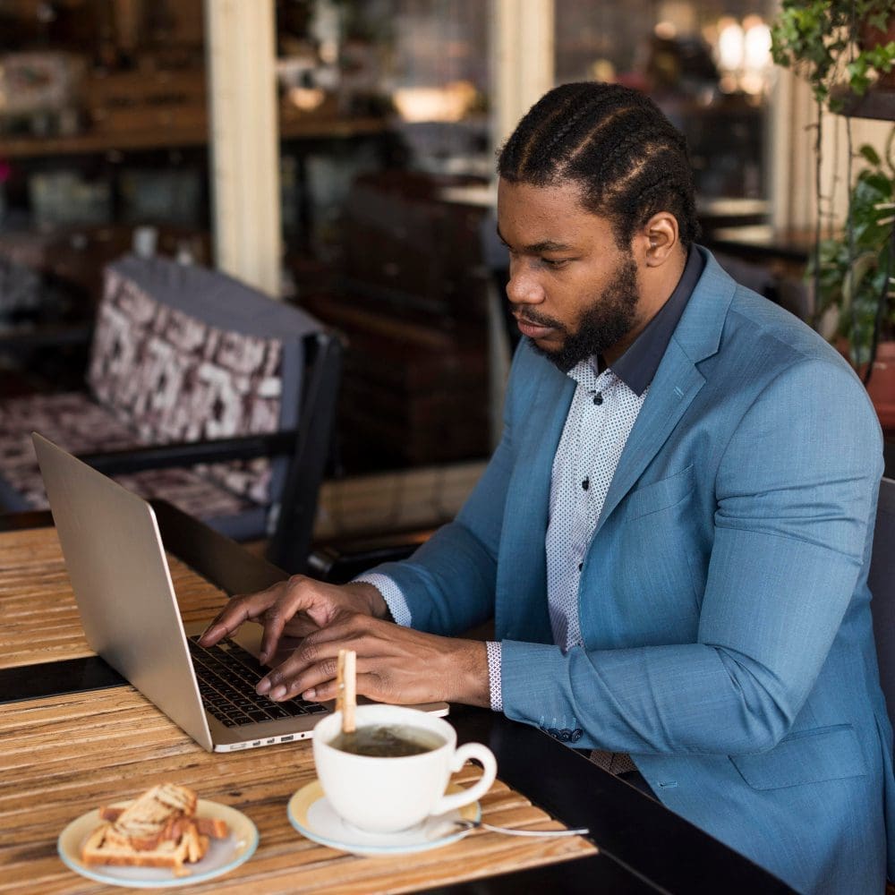 A man of African descent utilizing a laptop at a local cafe.